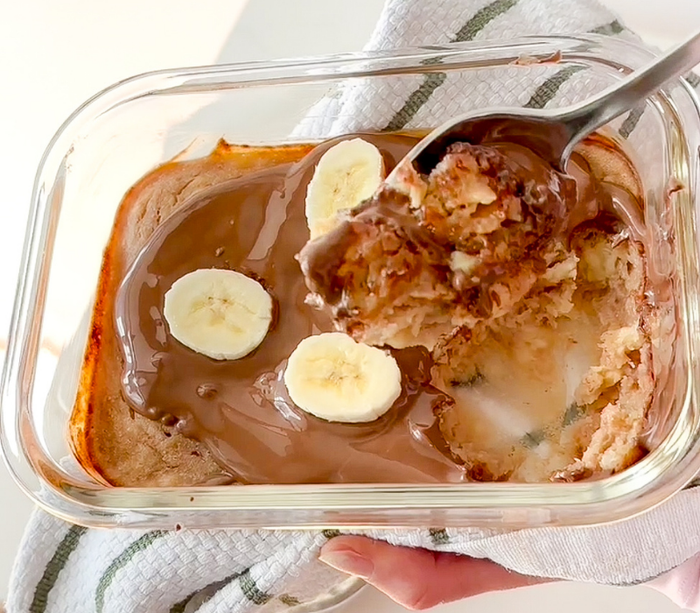 Close up image of a Banana Bred Dessert Bowl with melted chocolate and banana slices on top, and a spoon digging in.