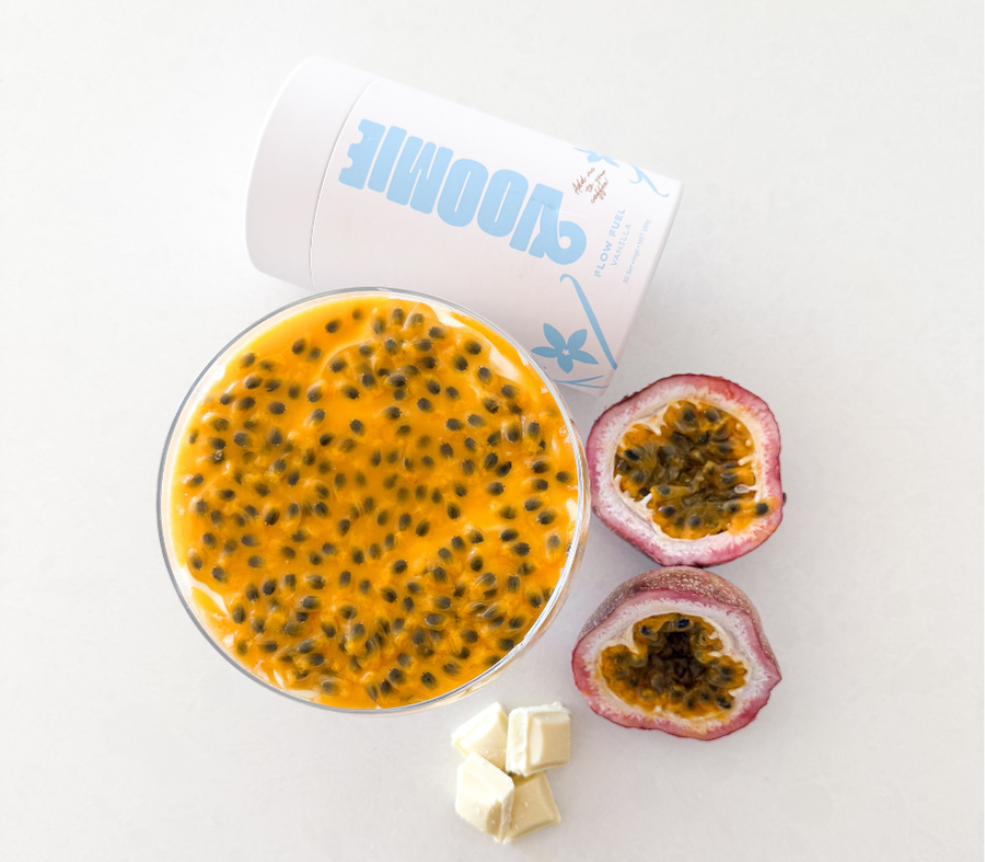 Above shot of overnight oats with a layer of white chocolate and passionfruit on top, with a cylinder of  Voomie Flow Fuel, a halved passionfruit and some white chocolate placed around the bowl.